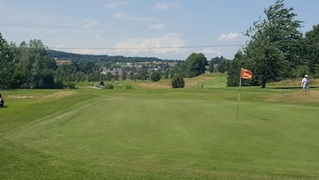 Un campo de golf con una bandera, árboles y una vista distante de casas.