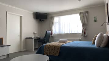 A hotel room with a bed, a desk, a chair, a small table, and a TV on the wall.