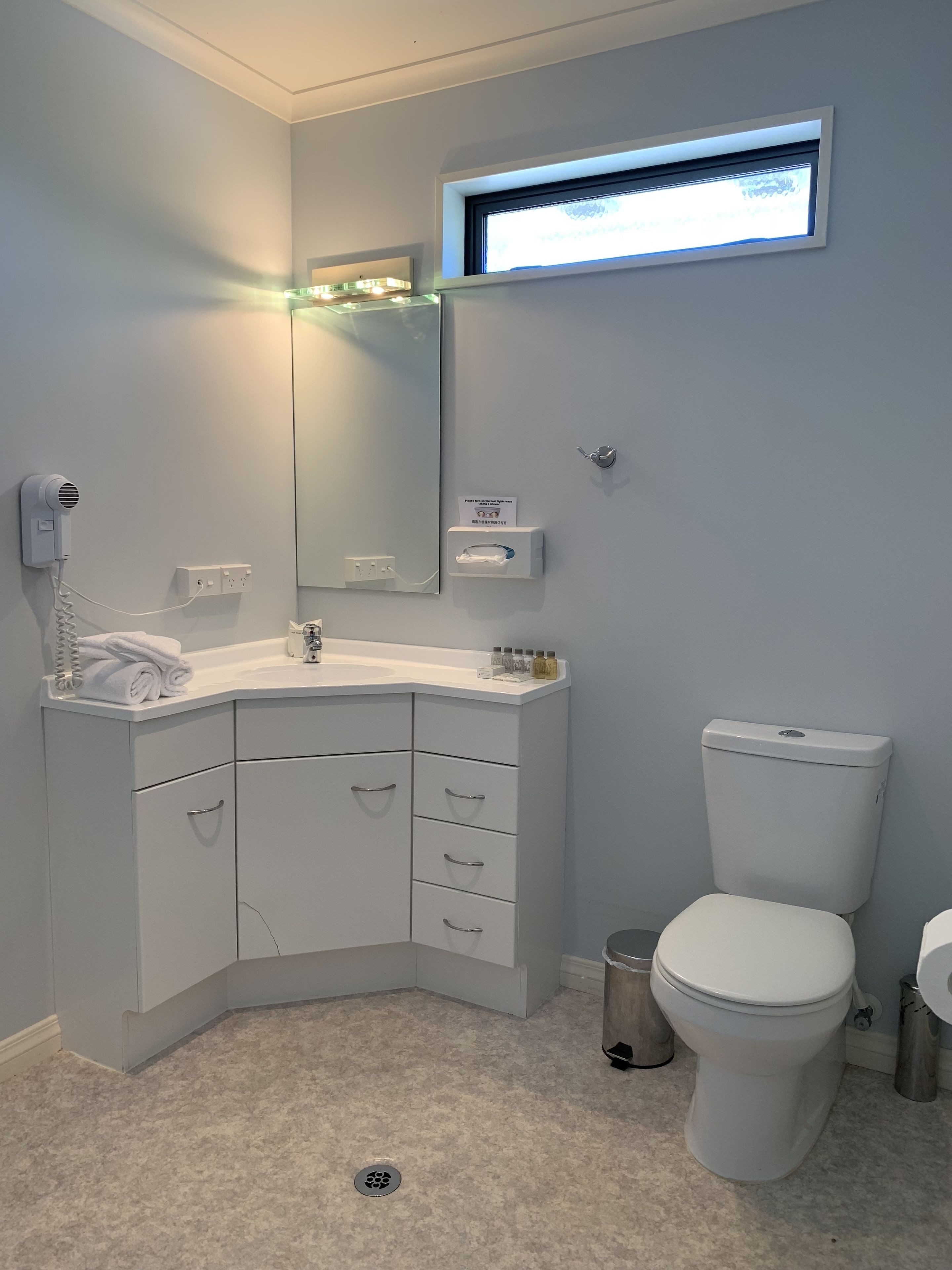 Une salle de bain moderne avec un lavabo d’angle, des toilettes, un miroir et un sèche-cheveux.