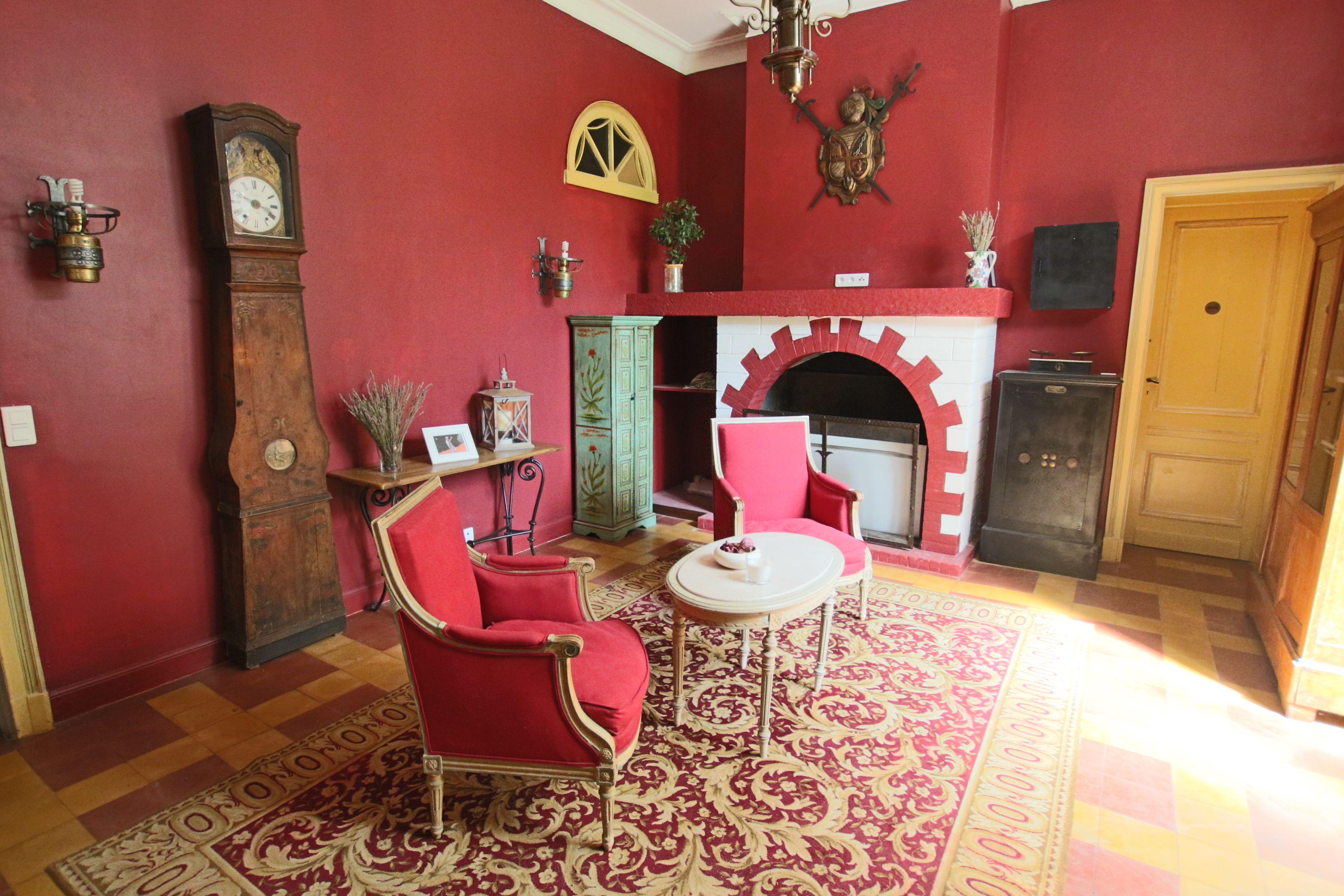A room with a red wall, a fireplace, a clock, and red furniture.