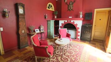 A room with a red wall, a fireplace, a clock, and red furniture.