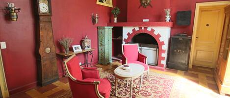 A room with a red wall, a fireplace, a clock, and red furniture.