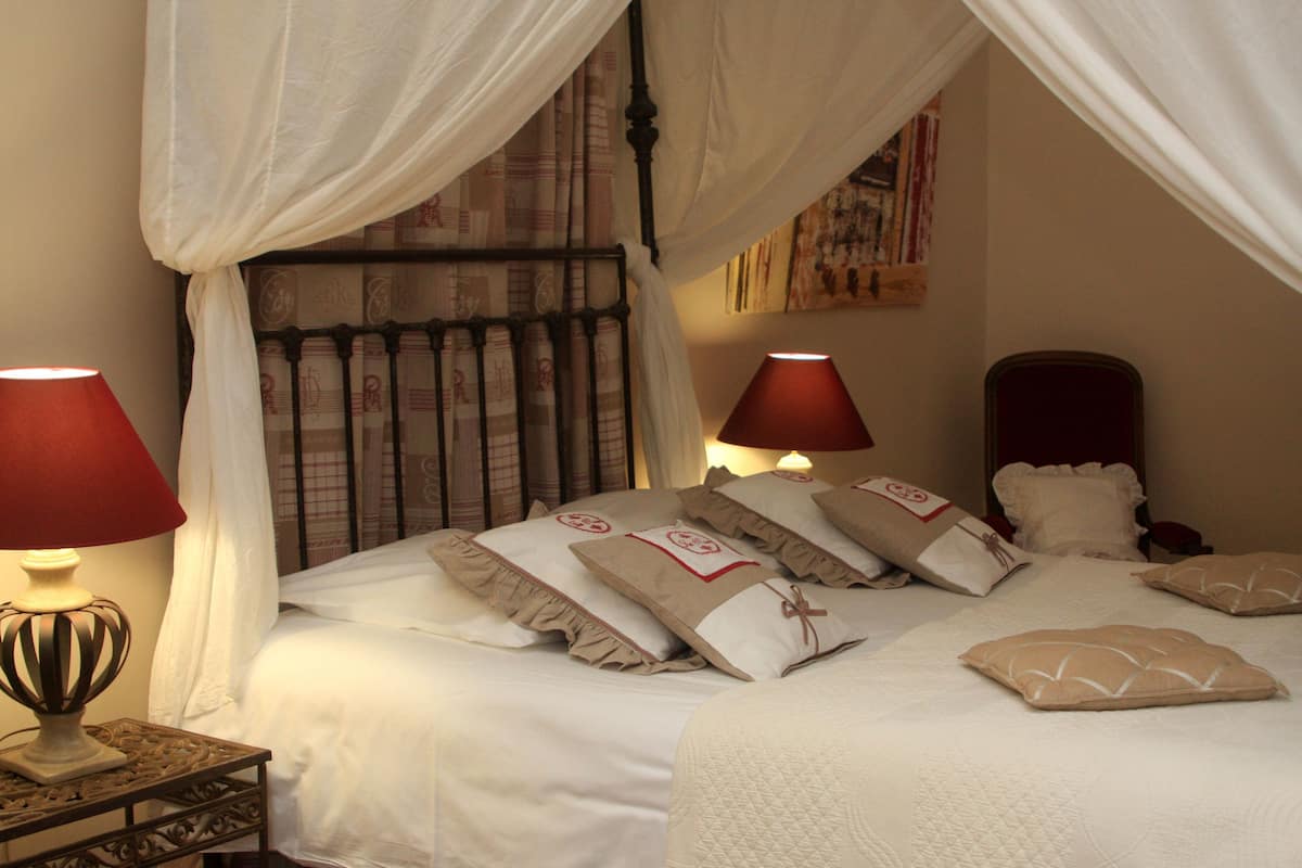 A neatly made bed with white linens and multiple pillows, a bedside table with a lamp, and a canopy bed with draped fabric.