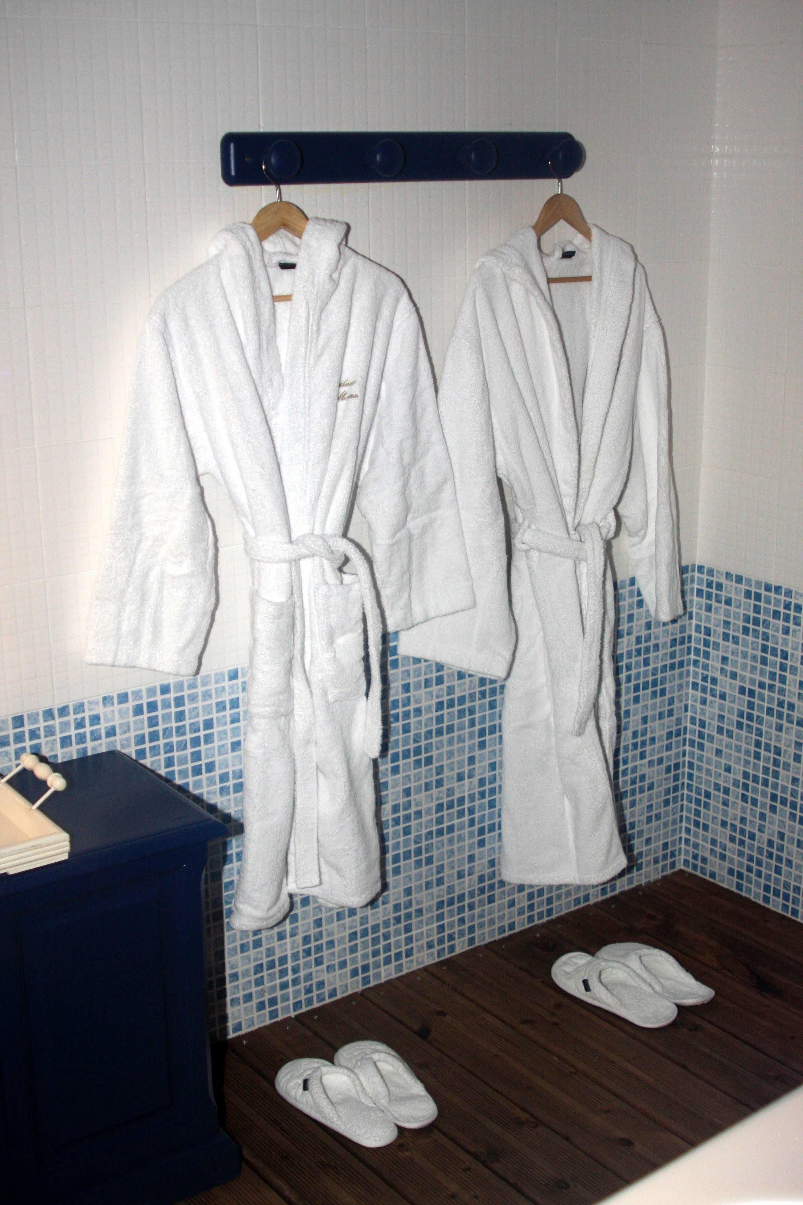Two white bathrobes hanging on a rack in a bathroom with blue mosaic tiles and wooden flooring.