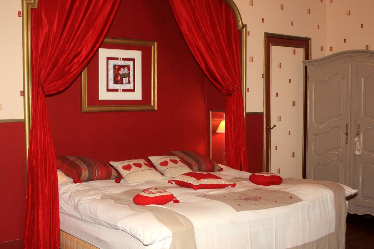 A bedroom with a four-poster bed, red curtains, and a white wardrobe.