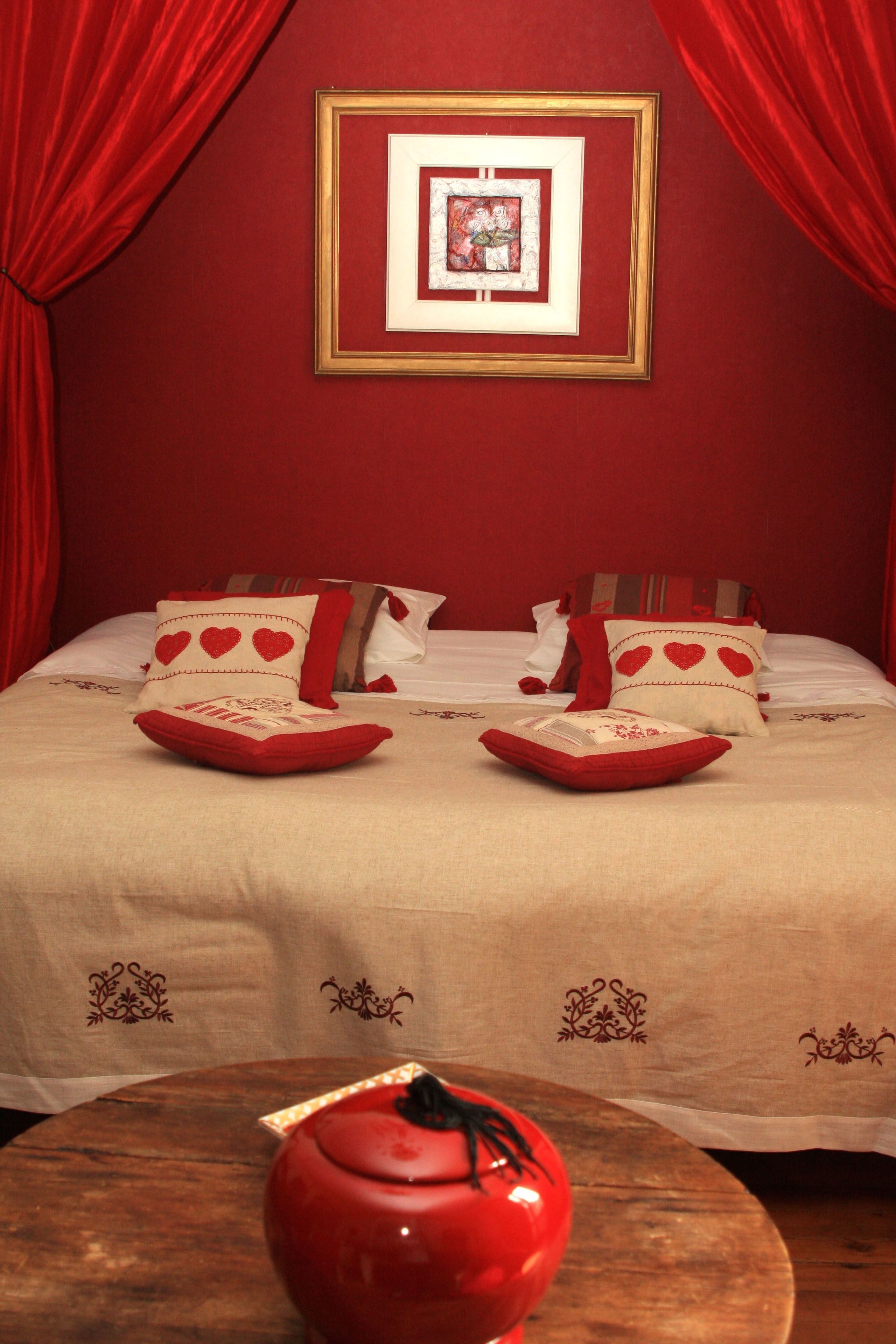 A hotel room with a red and white themed bed, a framed picture on the wall, and a red teapot on a wooden table.