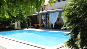 Una piscina con un porche cubierto, una mesa pequeña y sillas.