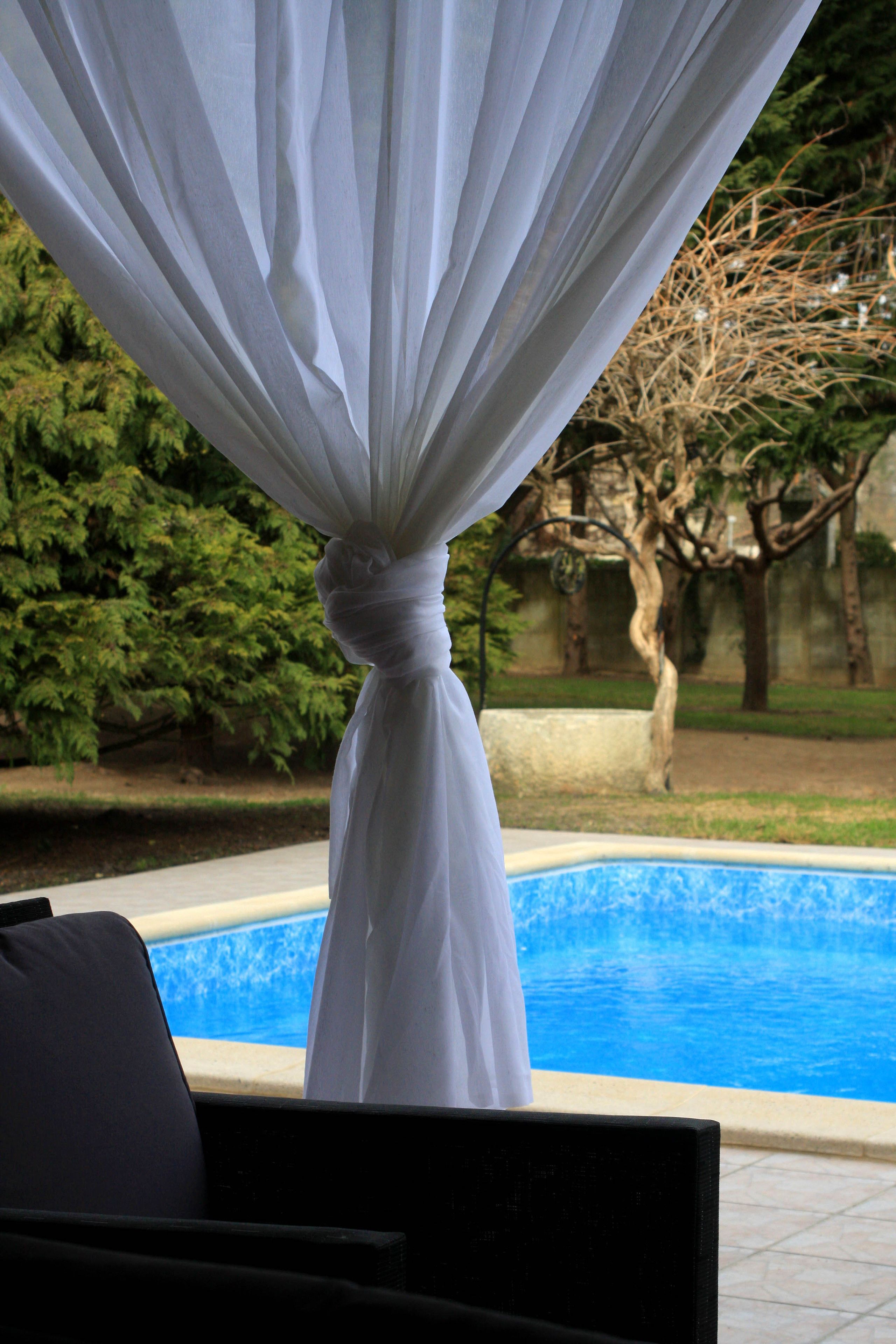 Un espace aménagé au bord de la piscine, avec un rideau blanc et une chaise.