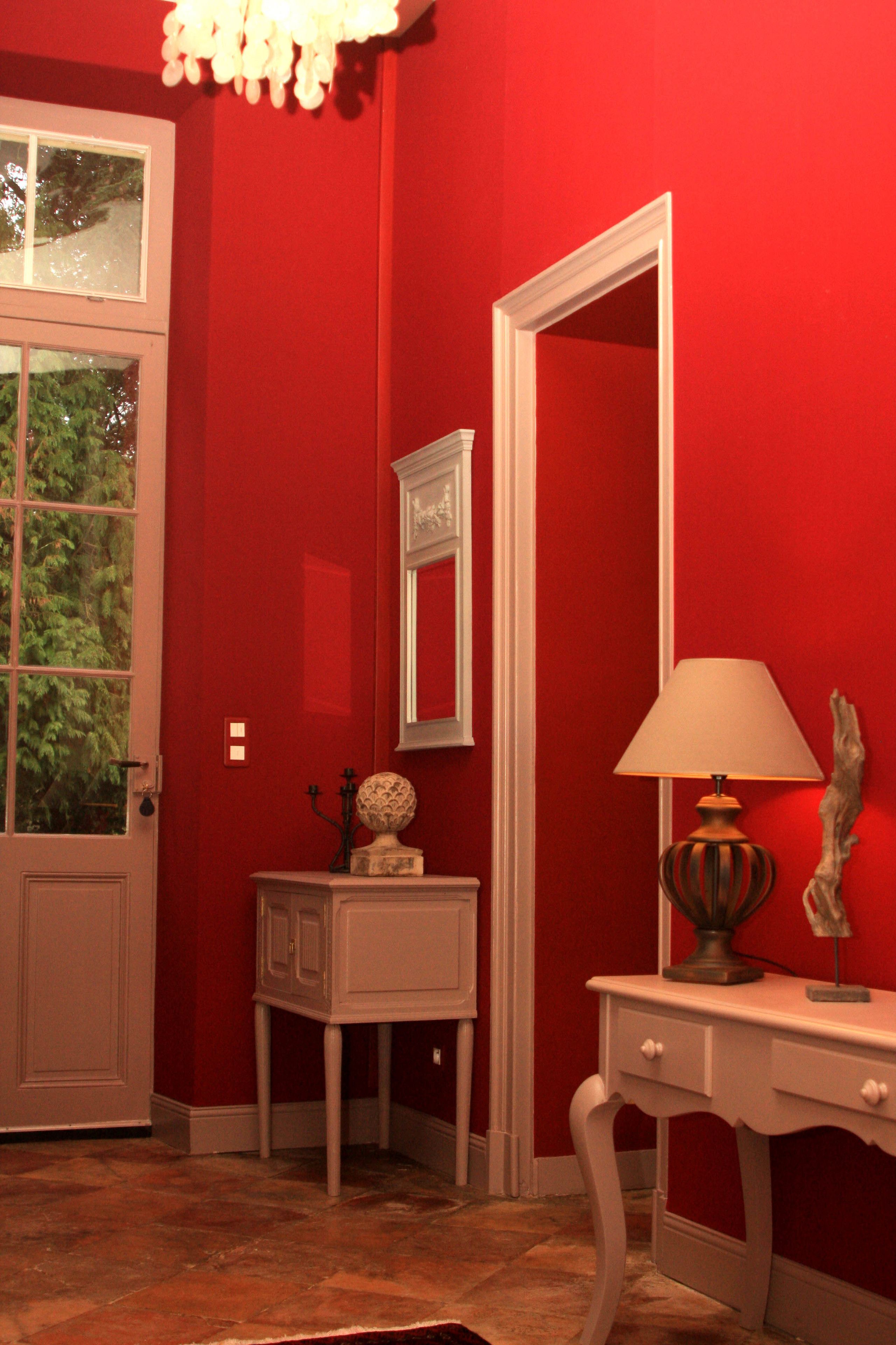 Quarto com paredes vermelhas, porta branca, mesa branca com abajur e espelho na parede.