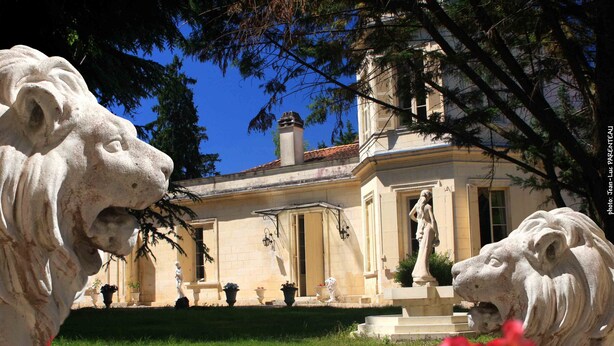 Un edificio clásico con una estatua central, una fuente y dos estatuas de leones al frente.