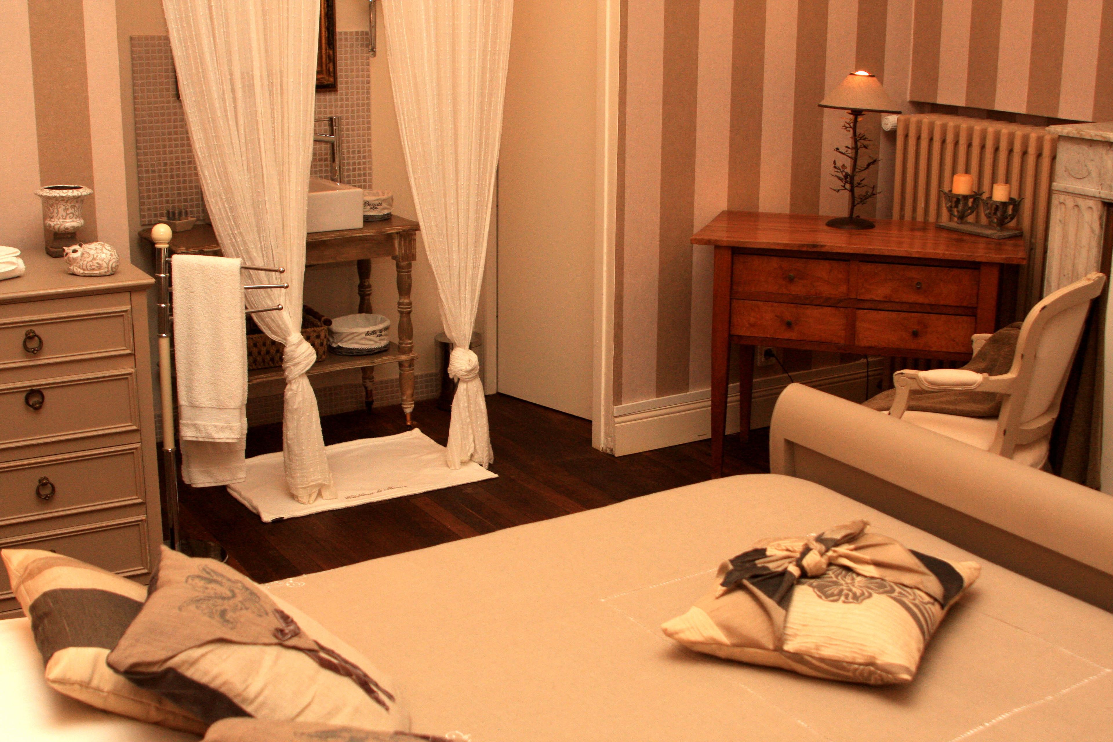 A hotel room with a bed, a wooden dresser, a chair, a vanity with a mirror, and a window with curtains.