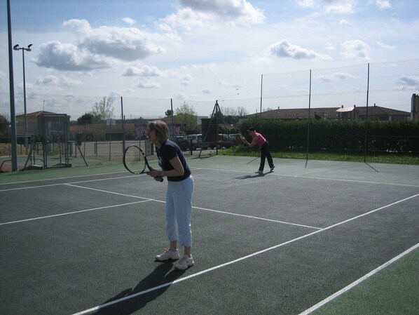 An outdoor tennis court with a net, two players, and a fence. - Château la Moune (Montussan)