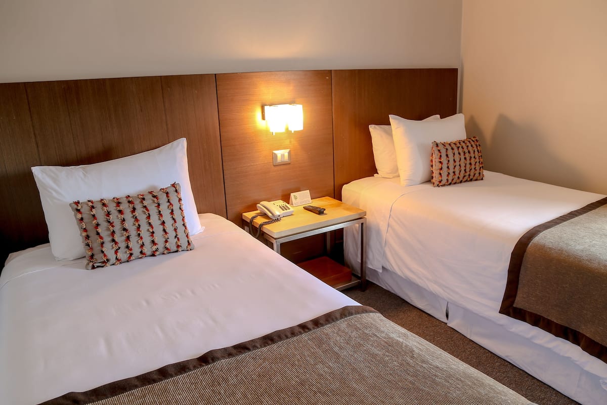 Une chambre d’hôtel avec deux lits, une table de chevet avec un téléphone et une lampe fixée au mur.