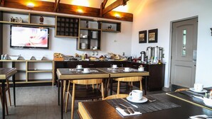 Um restaurante acolhedor com mesas e cadeiras de madeira, uma televisão na parede e prateleiras com louças e temperos.