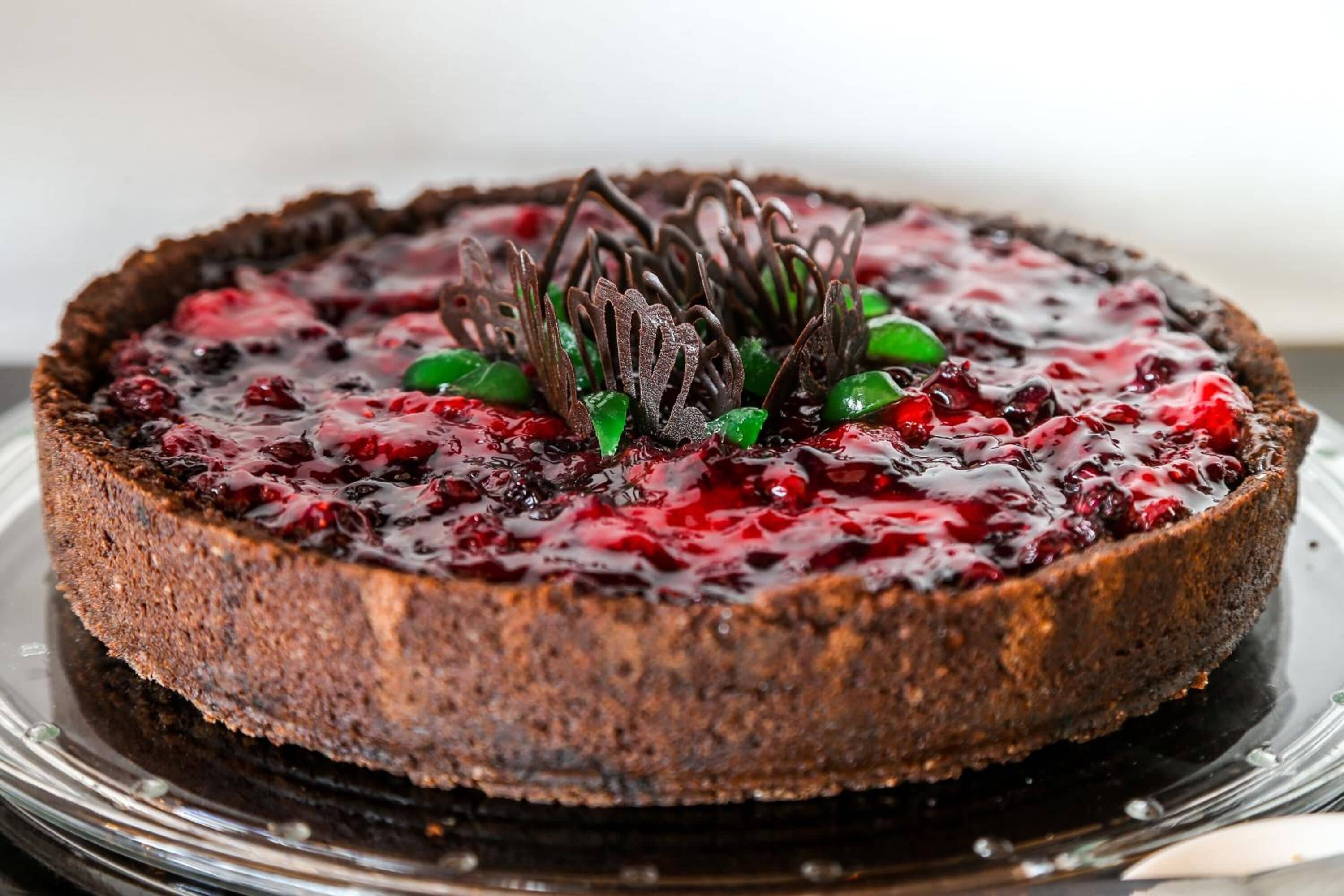 Un pastel redondo con corteza oscura, cubierto con un puré de frutos rojos y detalles de chocolate decorativos.