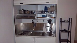 A compact kitchen with a sink, stove, and shelves for utensils and dishes. - Milos Apartments (Kassandra)
