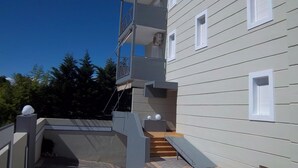 A multi-story building with a balcony, a staircase, and a small outdoor area with a bench. - Milos Apartments (Kassandra)