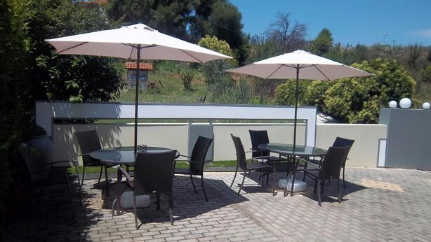 An outdoor patio with two round tables, four chairs, and two large umbrellas. - Milos Apartments (Kassandra)
