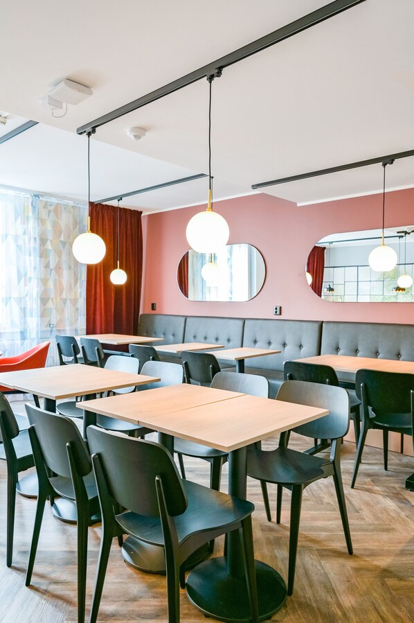 Interior de restaurante moderno con mesas de madera, sillas negras, pared de acento roja e iluminación colgante.