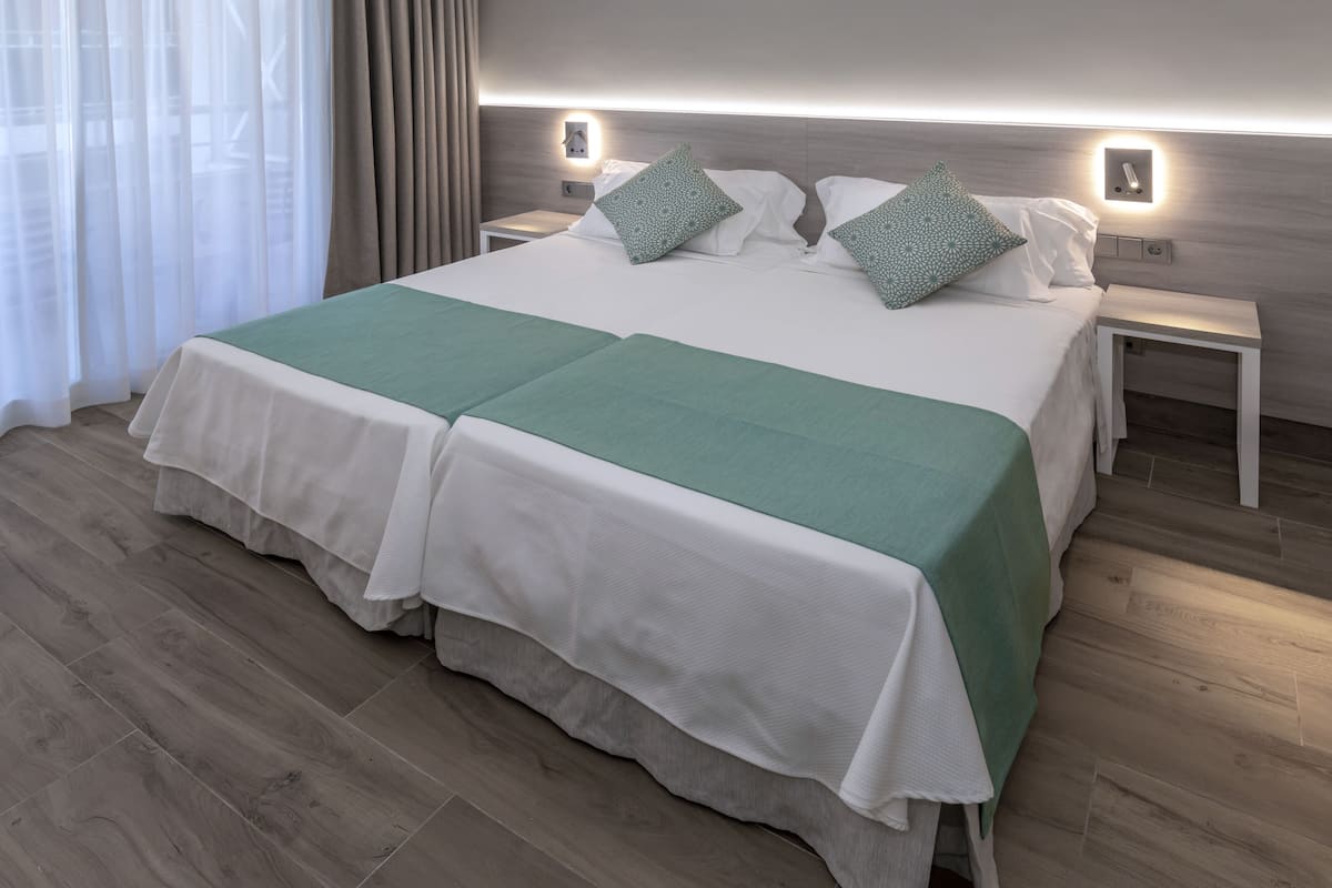 Una cama doble con colcha verde y blanca, dos almohadas a juego y dos mesitas de noche con lámparas de pared.