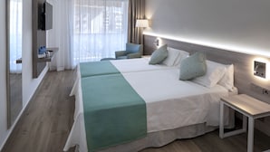 Ein Hotelzimmer mit einem großen Bett, einem Nachttisch, einem Sessel, einem an der Wand montierten Fernseher und einem Fenster mit Vorhängen.