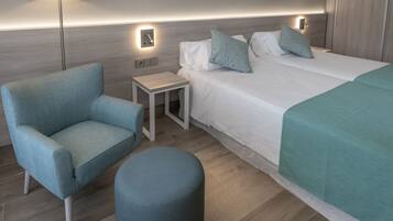 A hotel room with a bed, a chair, a small table, and a lamp.