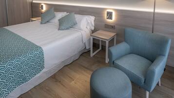 Habitación de hotel ordenada con una cama grande, un sillón azul, una mesita y una lámpara.