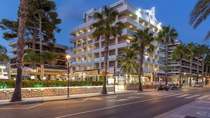 Ein mehrstöckiges Hotel mit Balkonen, Palmen und Sitzgelegenheiten im Freien.