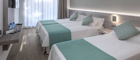 A hotel room with two beds, each with a green and white bedspread, a bedside table, a nightstand, and a wall-mounted TV.