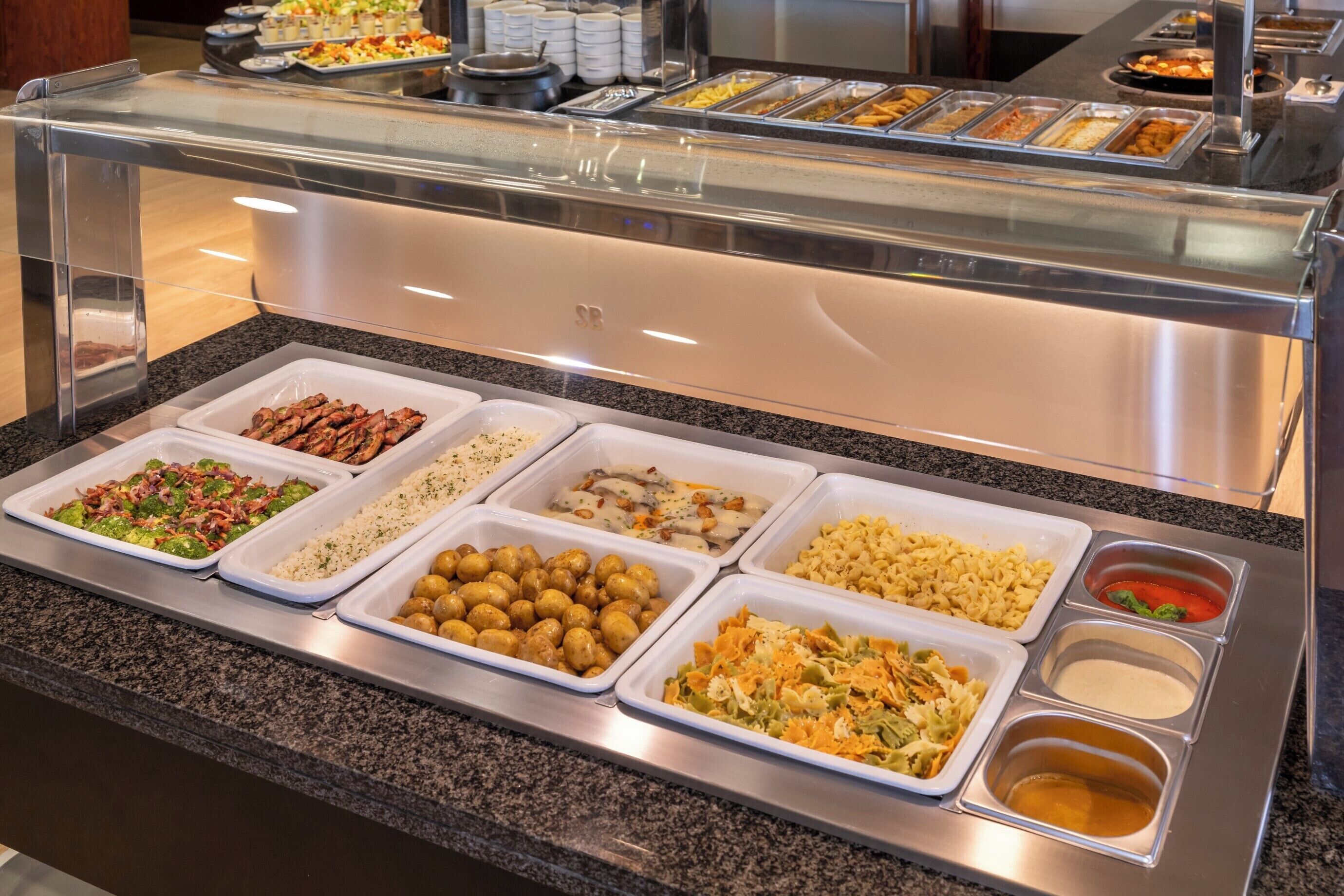 Een buffet met diverse gerechten, waaronder salades, pasta en rijst.