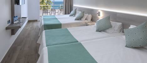 A hotel room with two beds, a TV, a balcony with a view of the ocean, and a table with chairs.