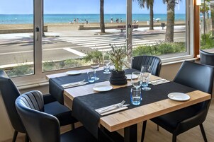 Comedor con vista a la playa, con una mesa dispuesta con platos, vasos y cubiertos.