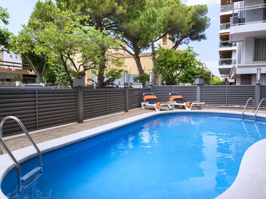 Una piscina con una escalera de metal, dos sillas de descanso y una valla.