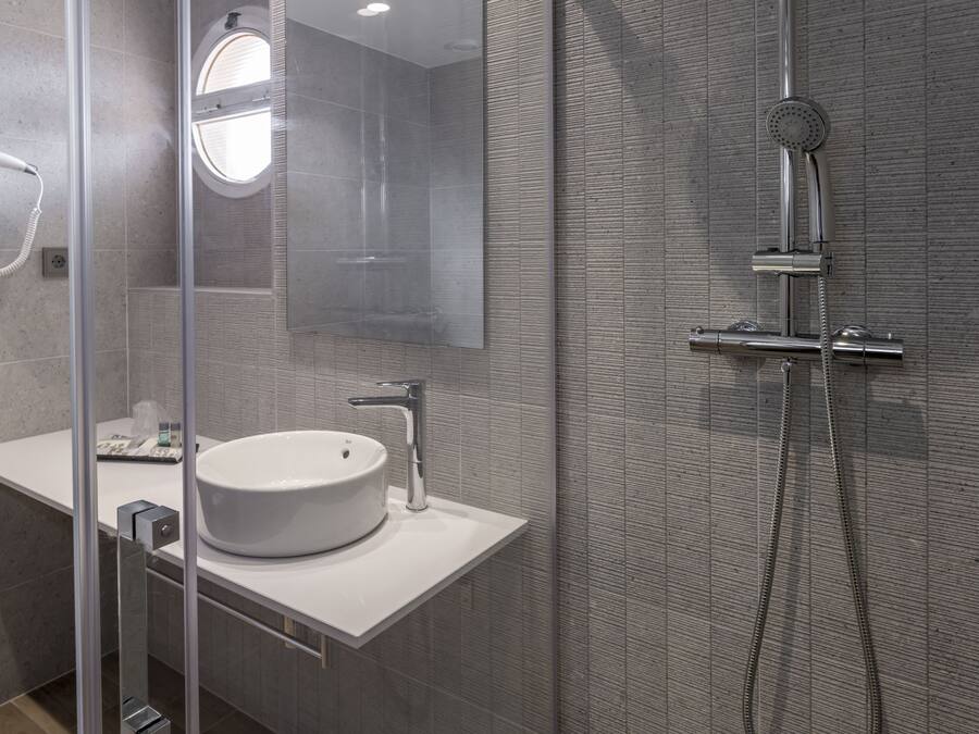 Un baño moderno con ducha de vidrio, lavamanos blanco y cabezal de ducha de mano.