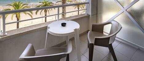 A balcony with a view of the beach, two chairs, a small table, and a bowl.