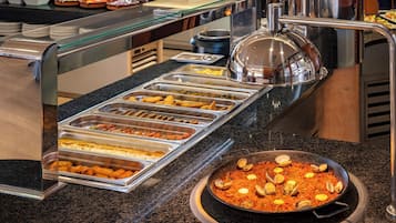 Een buffet met verschillende gerechten, waaronder een grote pan zeevruchtenpaella.
