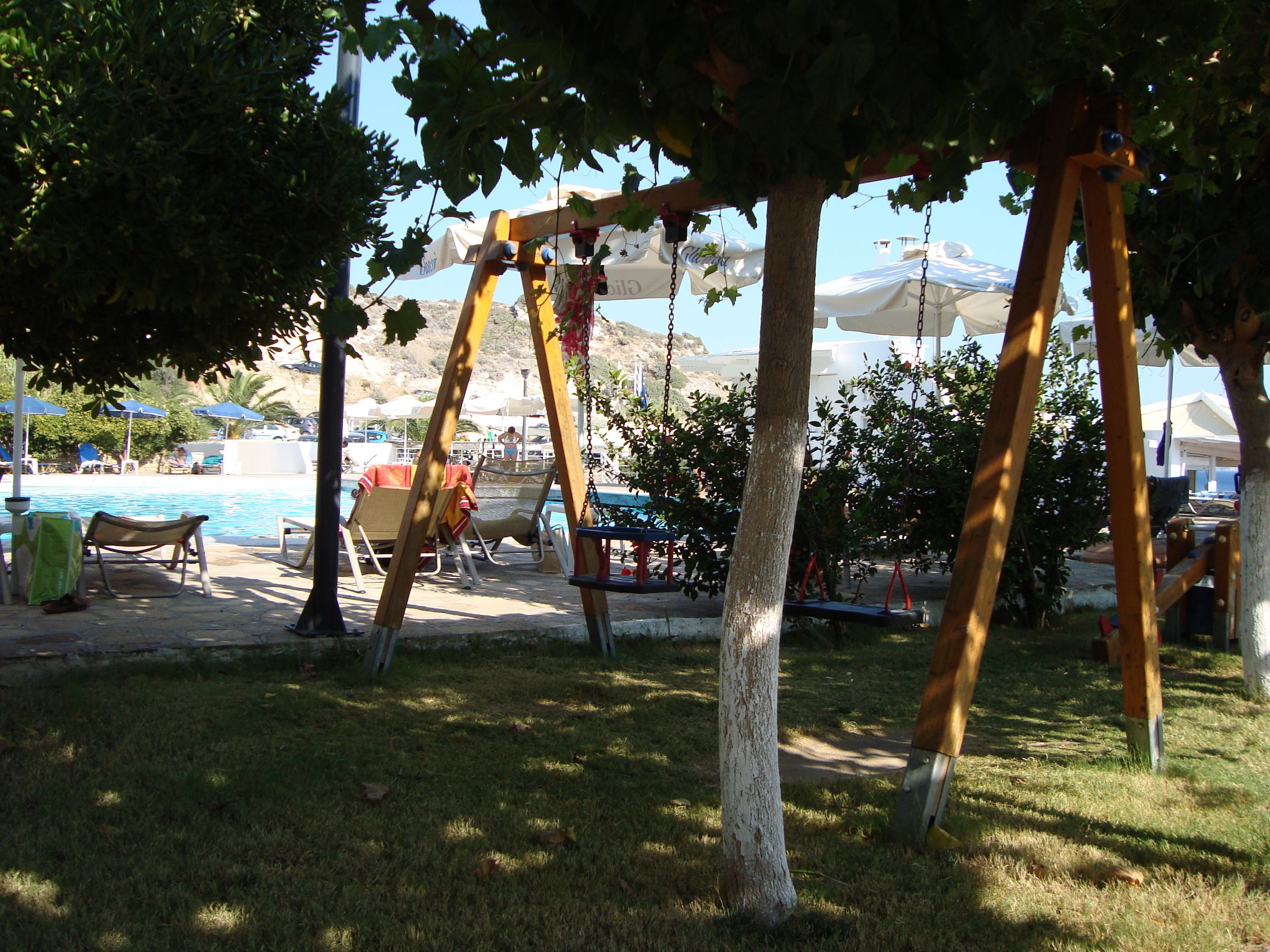 Un área junto a la piscina con sillones reclinables, un columpio y sombrillas.
