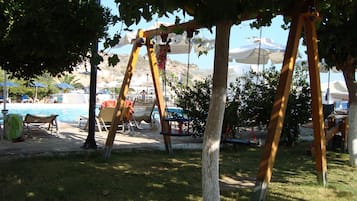 Un área junto a la piscina con sillones reclinables, un columpio y sombrillas.