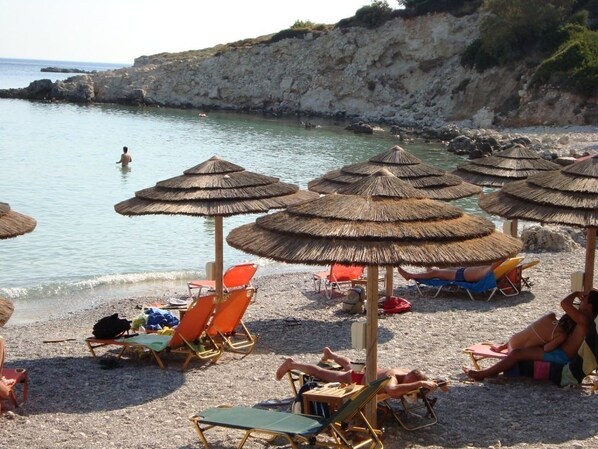 A beach with thatched umbrellas, sun loungers, and a rocky coastline. - Glicorisa Beach (Samos)