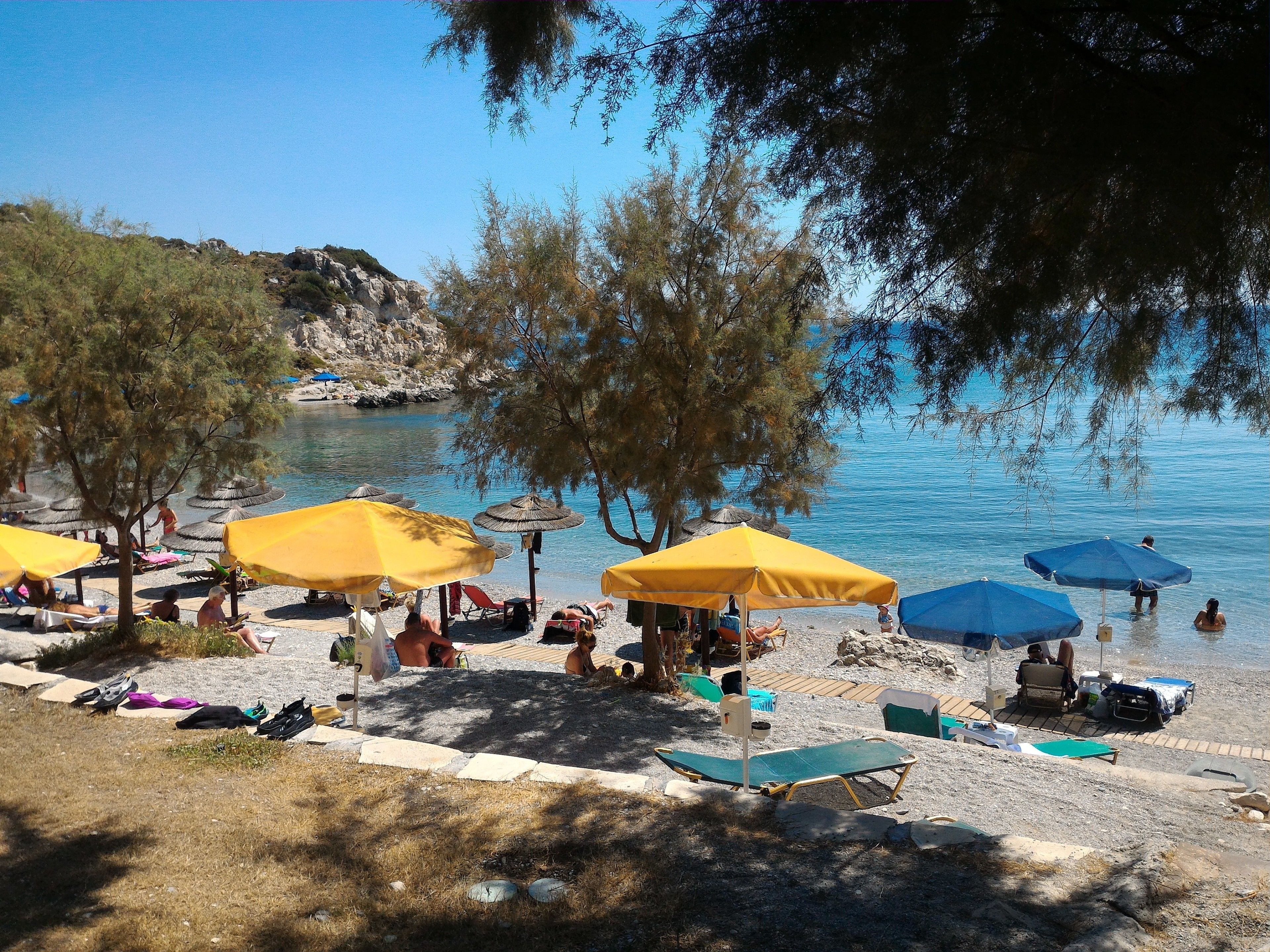 A beach with yellow and blue umbrellas, sun loungers, and a rocky shoreline.