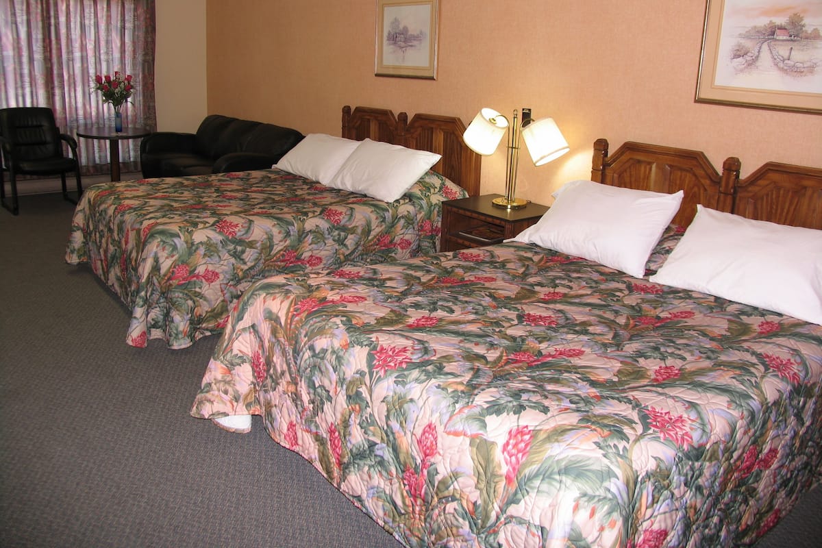 Habitación de hotel con dos camas, una silla, una mesita y una lámpara.