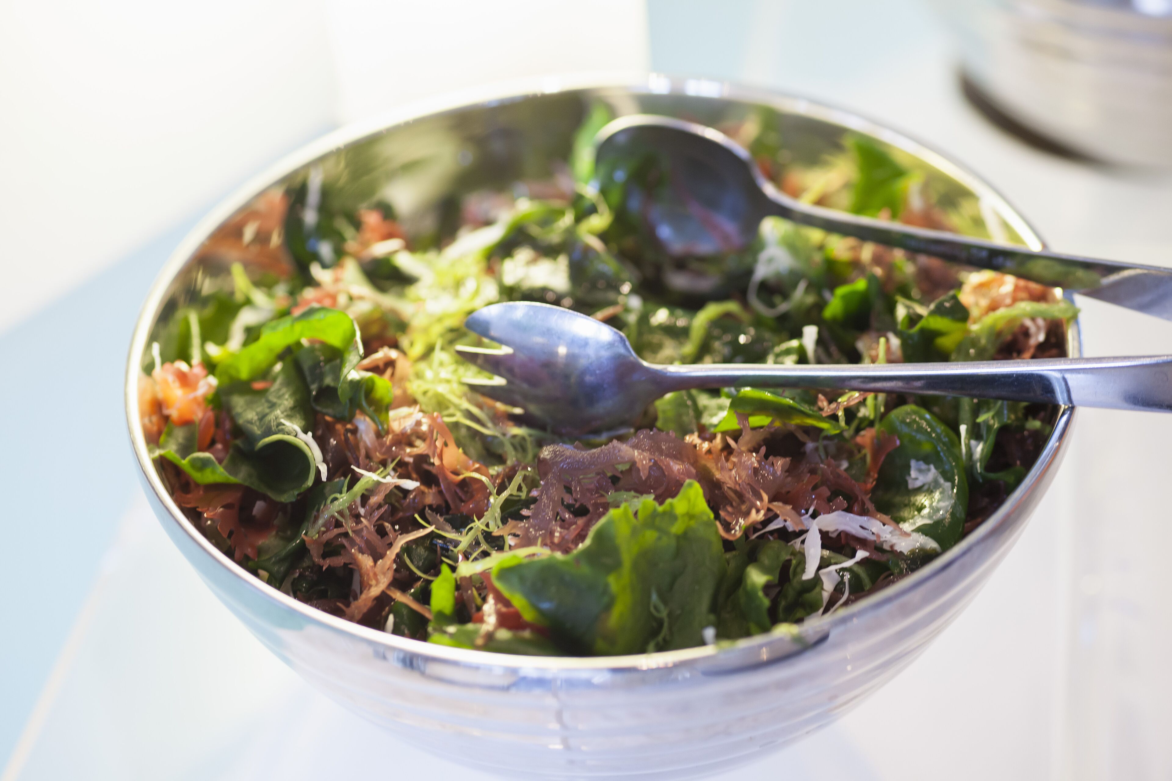 Eine Salatschüssel mit verschiedenen Blattsalaten und Beilagen, dazu liegen zwei Löffel.