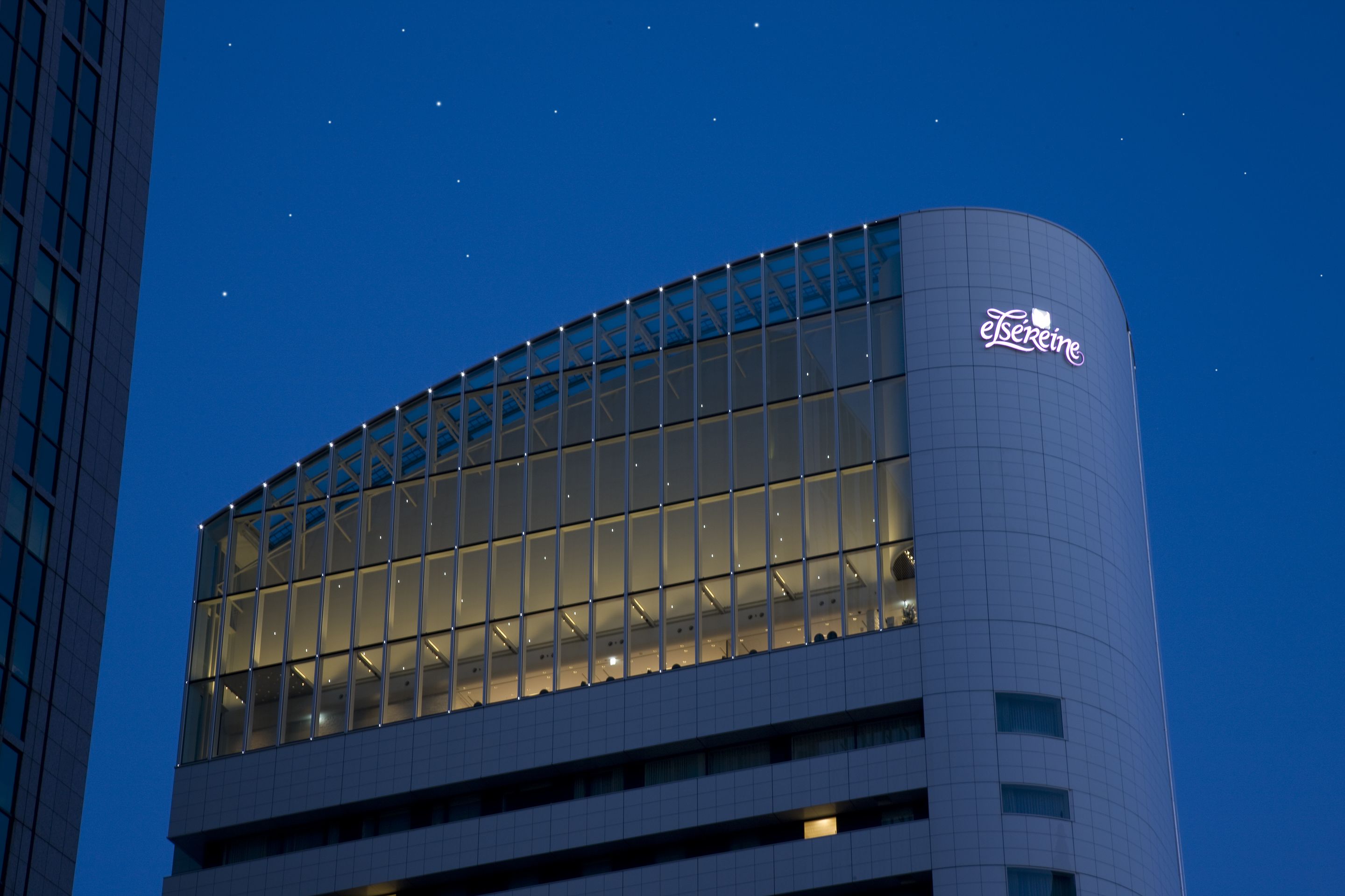 Un edificio moderno con fachada curva, amplios ventanales de vidrio y un cartel iluminado destacando.