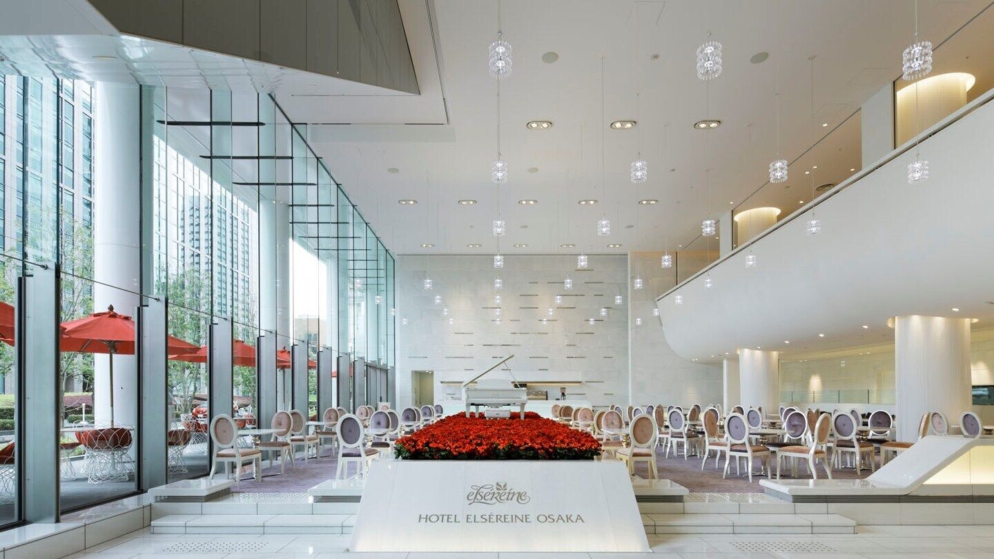 A hotel lobby with a grand piano, a reception desk, and a seating area with tables and chairs.