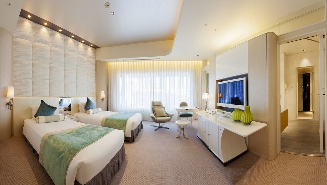 A hotel room with two beds, a desk, a chair, a TV, and a bathroom.