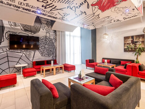 A modern lounge area with red and grey sofas, a flat-screen TV, and a wall with abstract art and signatures. - ibis Tanger City Center (Tangier)