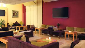 A modern hotel lobby with multiple seating areas, a flat-screen TV, and a large window with curtains.