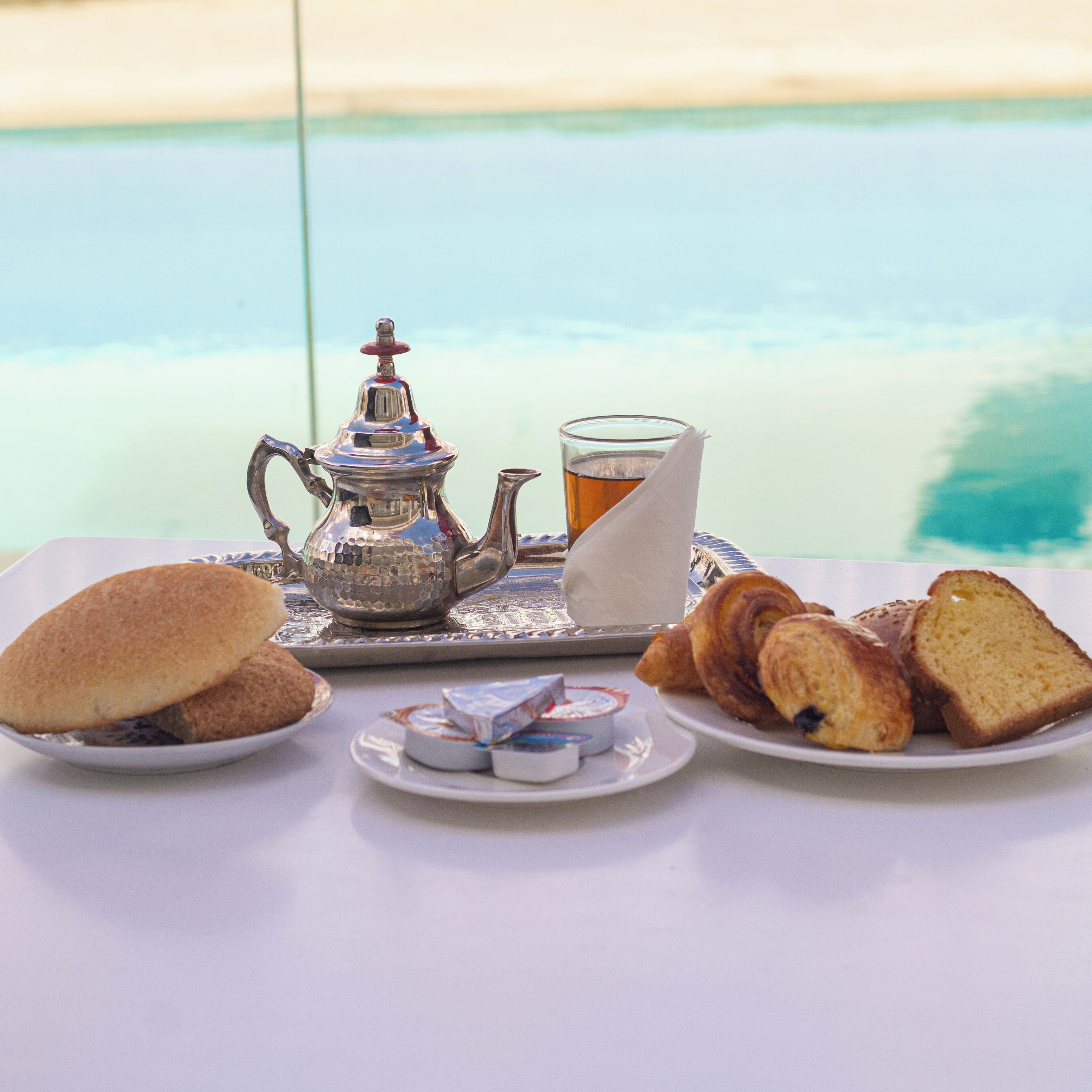 A table set with a teapot, a glass of tea, croissants, and a plate of bread.