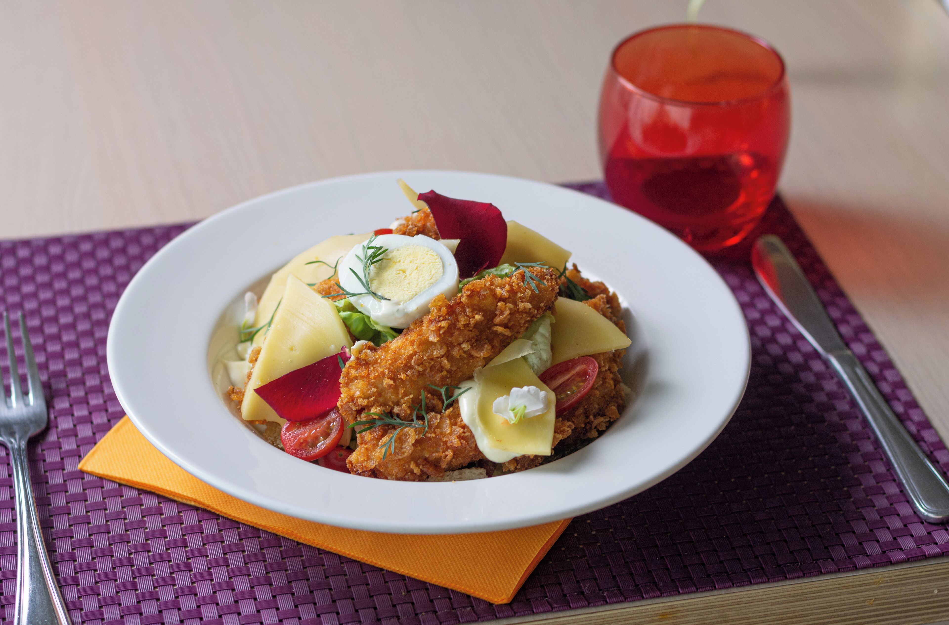 A plate of food with a fried item, vegetables, and a boiled egg on a white plate, accompanied by a red drink and cutlery on a purple mat.