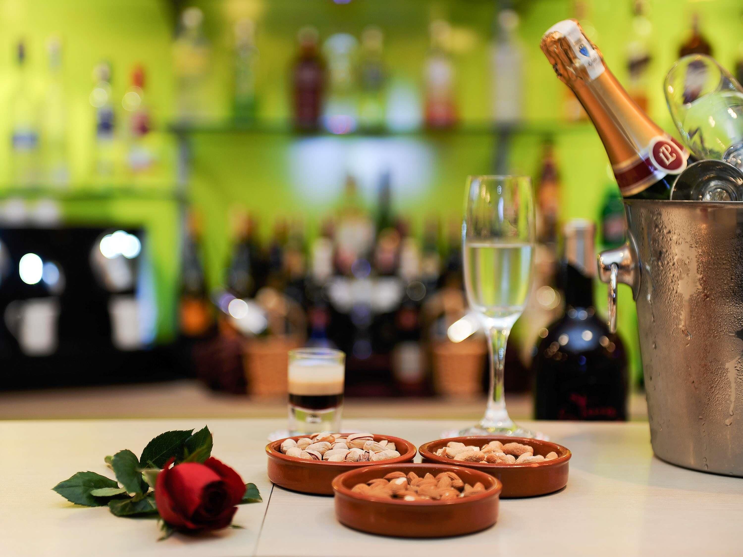 Un bar con una botella de champán, copas y recipientes con frutos secos.